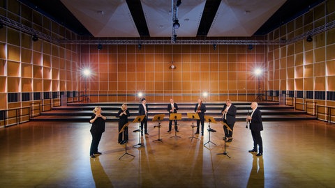 Musizierende mit Holzblasinstrumenten in einem Probensaal. Gemeinsam spielen sie das Stück 