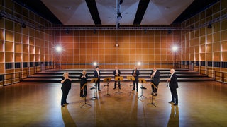 Musizierende mit Holzblasinstrumenten in einem Probensaal. Gemeinsam spielen sie das Stück "Canzone per Sonare" von Giovanni Gabrieli.