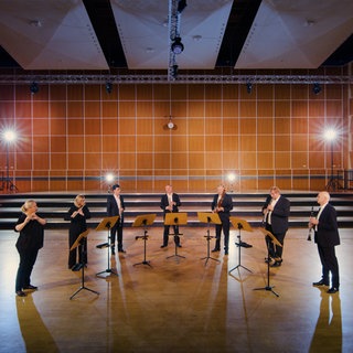 Musizierende mit Holzblasinstrumenten in einem Probensaal. Gemeinsam spielen sie das Stück "Canzone per Sonare" von Giovanni Gabrieli.