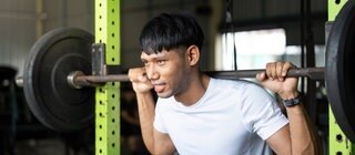 Junger Mann bei Kniebeugen mit einer Langhantel in einem Fitnessstudio