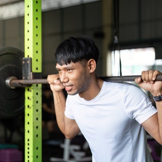 Junger Mann bei Kniebeugen mit einer Langhantel in einem Fitnessstudio