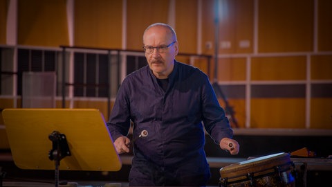 Ein Schlagwerker des Orchesters mit spannungsvollem Gesichtsausdruck kurz vor seinem Einsatz an einer Trommel.