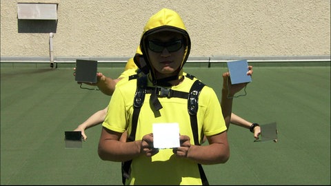 Eine Person steht auf einem grünen Rasen und hält einen Spiegel. Hinter ihm halten weitere Hände Spiegel in die Kamera.