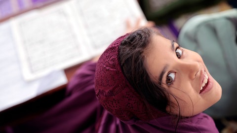 Junges Mädchen mit lila Kopftuch lächelt in die Kamera