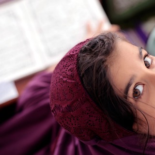 Junges Mädchen mit lila Kopftuch lächelt in die Kamera