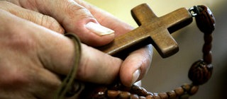 Mann hält Rosenkranz mit Kreuz in den Händen