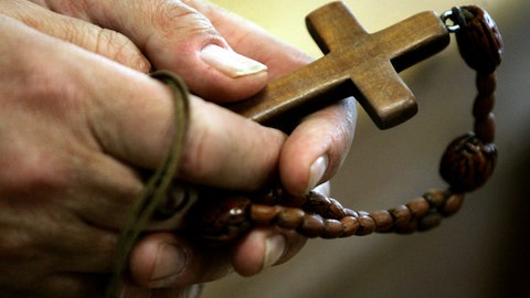 Mann hält Rosenkranz mit Kreuz in den Händen