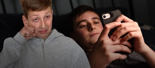 Trauriger Schüler im Vordergrund, im Hintergrund ein Kind am Smartphone