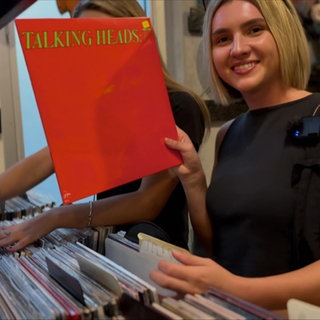Lily hält in einem Plattenladen eine LP in die Kamera