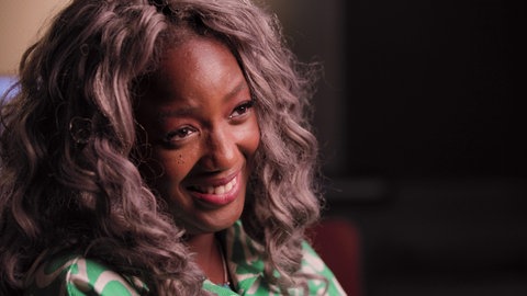 Eine Frau lacht während eines Interviews, Kamerasicht von der Seite.