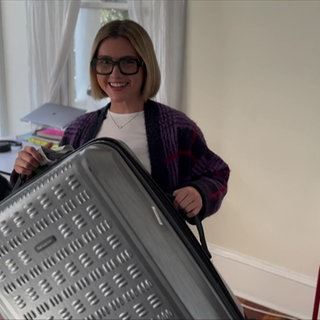 Lily hält einen Koffer in die Kamera