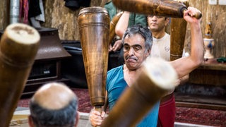 Männer schwingen schwere Holzkeulen