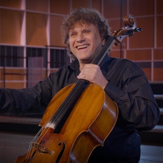 Ein Mann beendet freudestrahlend ein Musikstück auf einem Violoncello.  Das Instrument gehört zur Gruppe der Streicher.