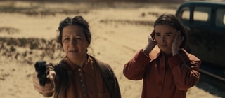 Spielszene: Golda Meir will ihr Land Israel verteidigen. Sie macht Schießübungen in der Wüste; ihre Tochter steht neben ihr und hält sich die Ohren zu.