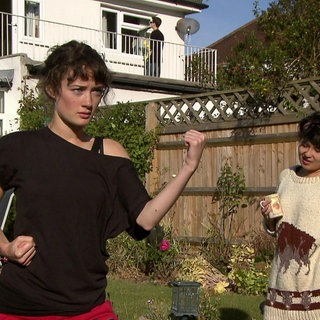 Zwei junge Frauen stehen im Garten. Die eine trinkt Kaffe, die andere trainiert Karate.
