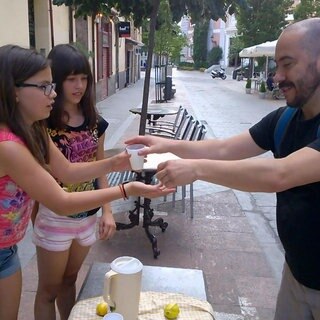 Zwei Mädchen verkaufen einem Mann Limonade.