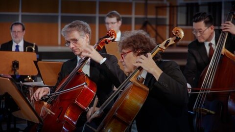 Orchestermitglieder spielen auf ihren Instrumenten, einem Cello und einem Kontrabass, das Stück Prélude aus Te Deum von Marc Antoine Charpentier.