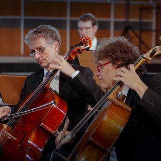 Orchestermitglieder spielen auf ihren Instrumenten, einem Cello und einem Kontrabass, das Stück Prélude aus Te Deum von Marc Antoine Charpentier.