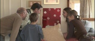 Eine Gruppe Menschen steht versammelt vor einem roten Bild. Eine rote Strumpfhandpuppe hat sich hier versteckt.