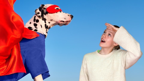 Links ein Hund im Superheldenkostüm mit großem rotem Umhang, rechts ein erstauntes Mädchen