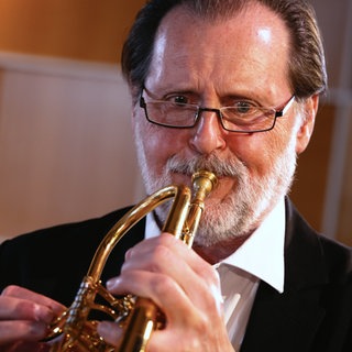 Ein Mann spielt Trompete. Er gehört mit seinem Instrument zur Gruppe der Blechbläser.