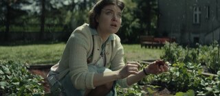 Spielszene: Hedwig Höß hockt im Erdbeerbeet im Garten neben dem KZ Auschwitz. Sie schaut zum Himmel, von dem es Asche aus dem angrenzenden KZ regnet.