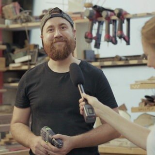 Stefanie mit Mikrofon in der Hand befragt eine Schreiner mit Akkuschrauber in der Hand