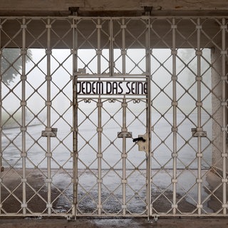 Der Schriftzug „Jedem das Seine“ auf dem weißen Gitter des Eingangs zum Konzentrationslagers Buchenwald. Der Ausdruck hat seit dem Nationalsozialismus eine negative Bedeutung.