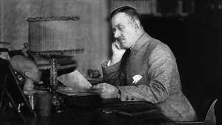 Thomas Mann sitzt an einem Schreibtisch und liest etwas