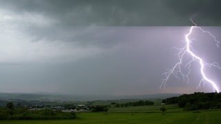 Blitz am blauen Himmel über Silhouette eines Hauses. Wie entsteht ein Gewitter? Was passiet bei Blitz und Donner?