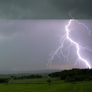 Blitz am blauen Himmel über Silhouette eines Hauses. Wie entsteht ein Gewitter? Was passiet bei Blitz und Donner?