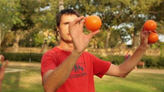 Ein Mann hält drei orange Jonglierbälle in die Luft.