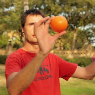 Ein Mann hält drei orange Jonglierbälle in die Luft.