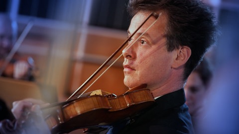 Ein Mann spielt Violine, im Hintergrund weitere Mitglieder der Streichergruppe eines Orchesters.