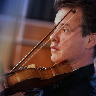 Ein Mann spielt Violine, im Hintergrund weitere Mitglieder der Streichergruppe eines Orchesters.