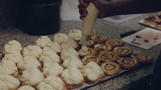 Eine Hand macht mit einer Spritztüte Sahnehäubchen auf Kekse