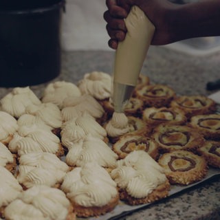 Eine Hand macht mit einer Spritztüte Sahnehäubchen auf Kekse