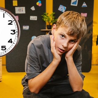 Schüler sitzt genervt in einem modernen Klassenzimmer, an der Wand hängt eine große Uhr
