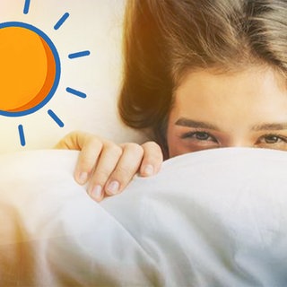 Es ist hell: Mädchen schaut unter der Bettdecke hervor. Was macht Sonnenlicht mit unserem Körper?