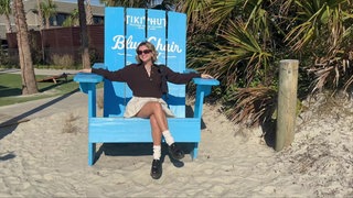 Lily sitzt in einem großen Holzstuhl an einem Strand