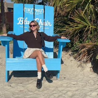 Lily sitzt in einem großen Holzstuhl an einem Strand