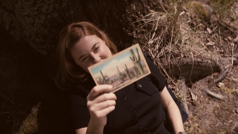 Spielszene: Joan Hinton hält lächelnd eine Postkarte in der Hand. Die Kernphysikerin arbeitet später am Manhattan-Projekt – der Entwicklung der Atombombe.