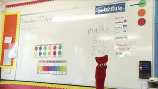 Eine Schultafel im Englischunterricht, davor eine rote Strumpfhandpuppe.