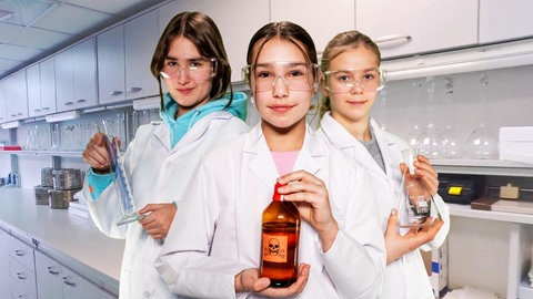 Im Hintergrund ein Labor, im Vordergrund drei Mädchen in Laborjacken und Schutzbrillen, die wissenschaftliche Instrumente halten