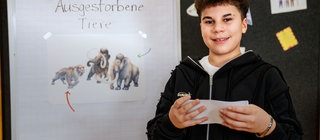 Ein Junge steht vor einer Tafel mit Karteikarten und wirkt entspannt und selbstbewusst