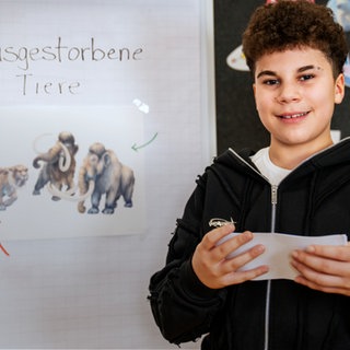 Ein Junge steht vor einer Tafel mit Karteikarten und wirkt entspannt und selbstbewusst