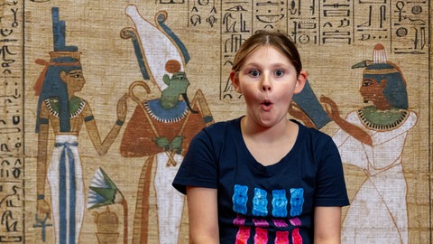 Im Hintergrund eine altägyptische Zeichnung auf Papyrus, im Vordergrund ein erstauntes Mädchen
