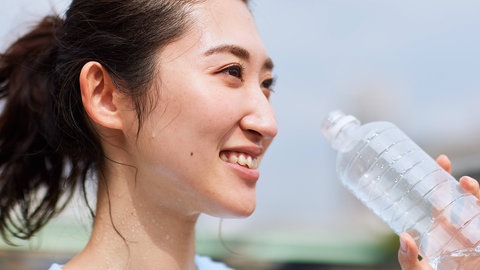 Junge Frau mit dunklen Haaren schwitzt und trinkt aus einer Wasserflasche