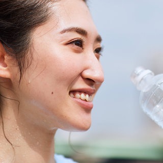 Junge Frau mit dunklen Haaren schwitzt und trinkt aus einer Wasserflasche